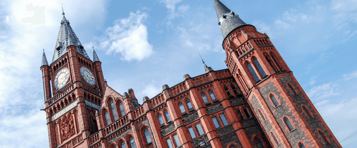 The Victoria Building at the University of Liverpool, an ornate red-brick Victorian Gothic clock tower and turret shot from below against a blue sky.