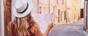 Female student holding a city map in a quiet European street – planning a low-cost travel adventure.