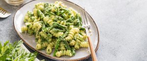 Bowl of pesto pasta on a table with a fork beside it cooked by a university student