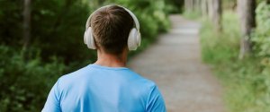 A student walking along a tree-lined path wearing headphones