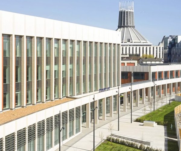 The LJMU Student Life Building, a modern glass-and-white curved façade, with Liverpool Metropolitan Cathedral's spire on the skyline behind.