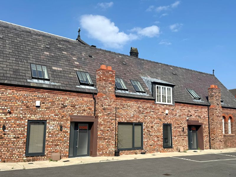 Completed conversion of a red-brick heritage building in Liverpool into student accommodation, with restored brickwork, new slate roof, rooflights and dormer window, and modern grey doors and shutters.