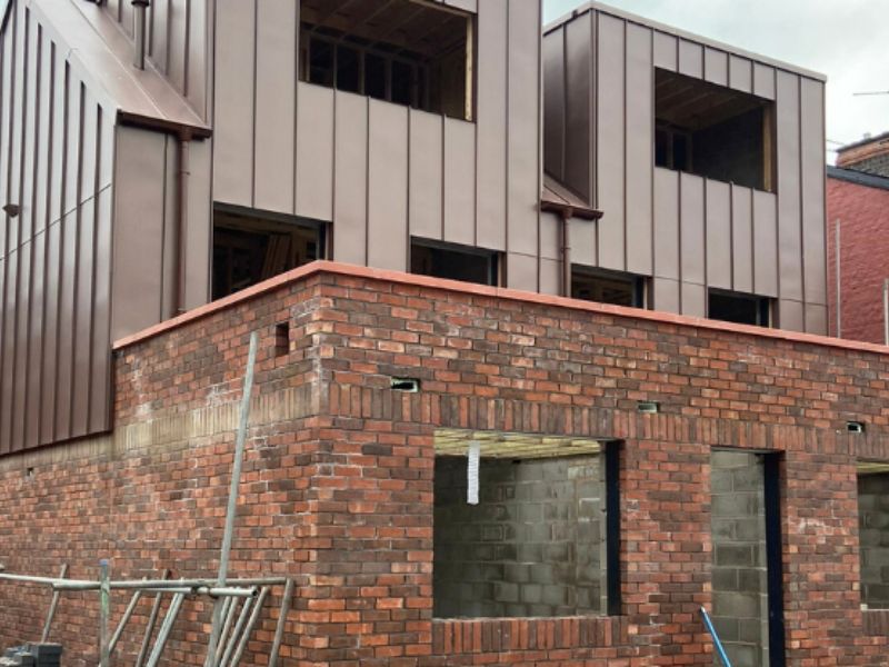 Rear of a modern student property under construction in Liverpool, with standing-seam metal cladding to the upper floors above a newly built red-brick ground floor, window openings awaiting frames.