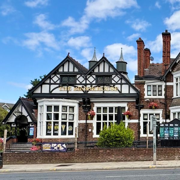 The Brook House, a large mock-Tudor pub with gabled brick-and-timber frontage on Smithdown Road, under a blue sky with scattered cloud.